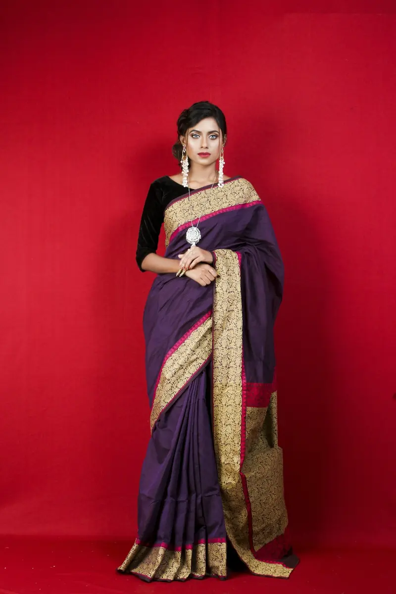 Woman in a purple silk saree standing at an angle against a red backdrop