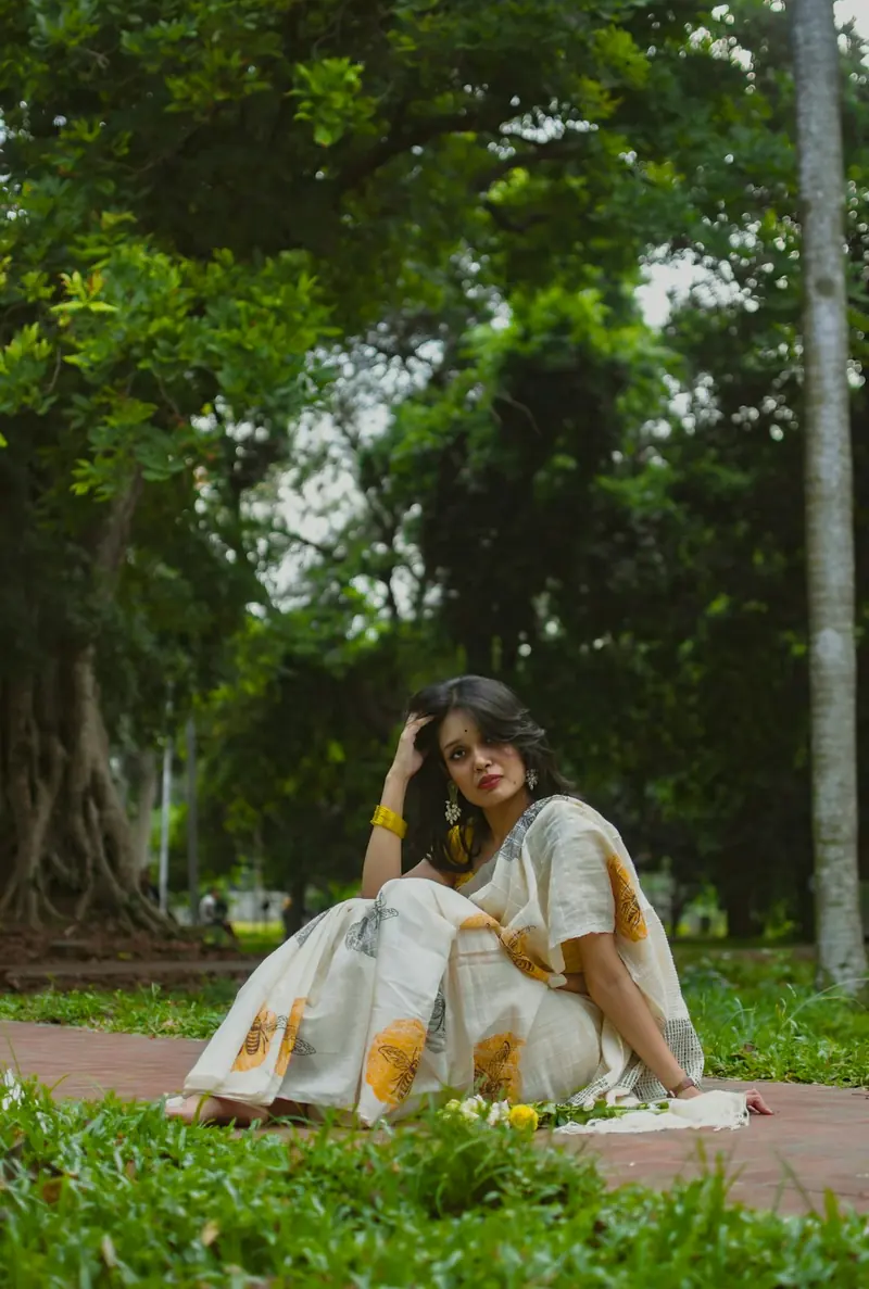 Woman in a white saree sitting on the grass with her legs to one side