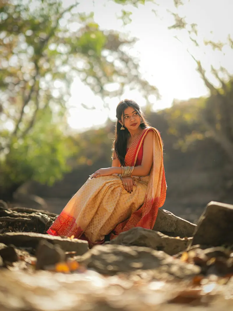 Woman in an orange and gold saree sitting on rocks in warm evening light