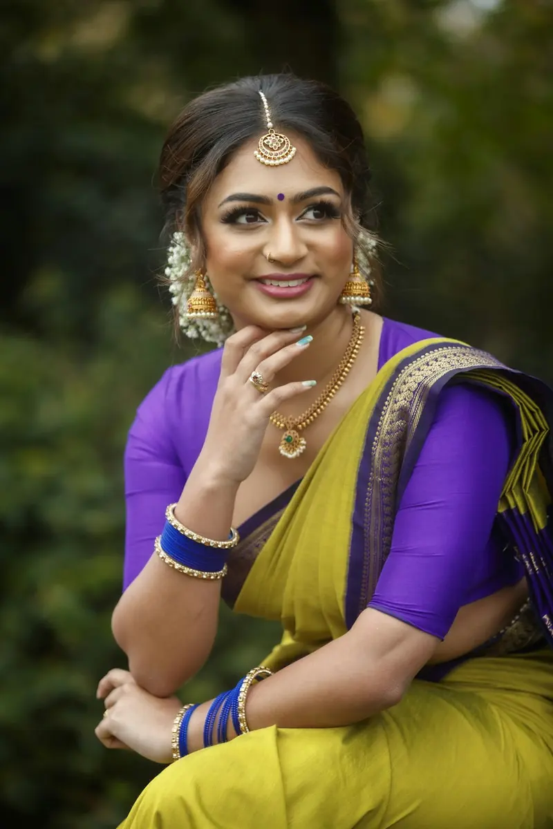 Woman in a yellow saree with a purple blouse sitting with her chin resting on her hand and smiling