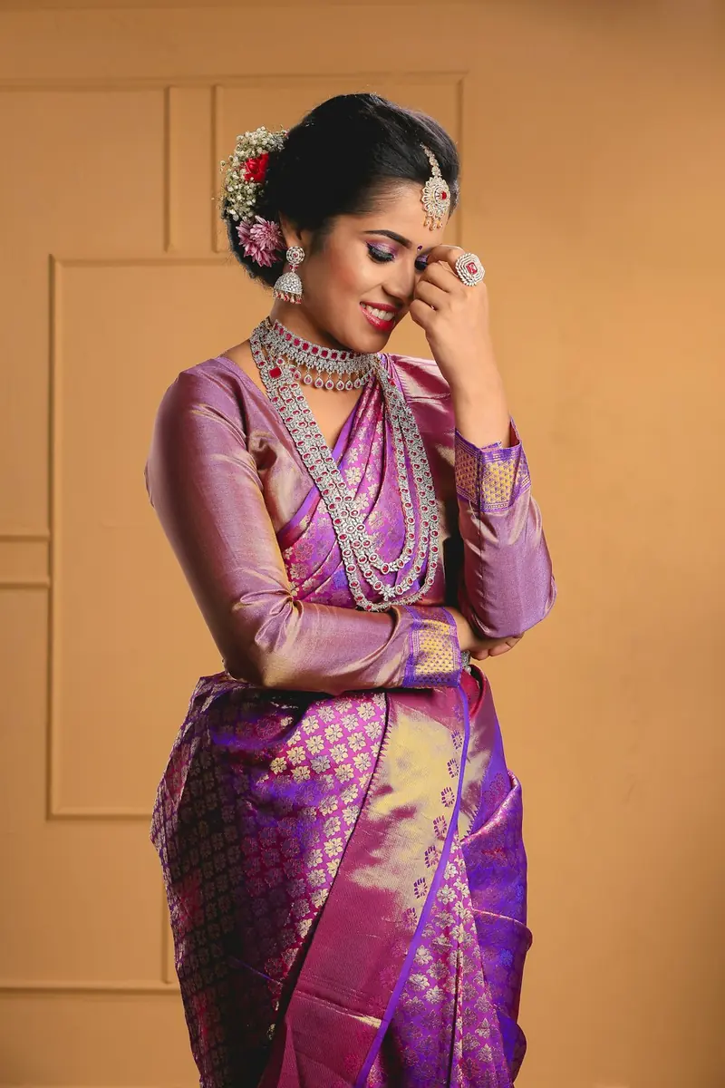 Woman in a purple and gold silk saree laughing with one hand at her forehead