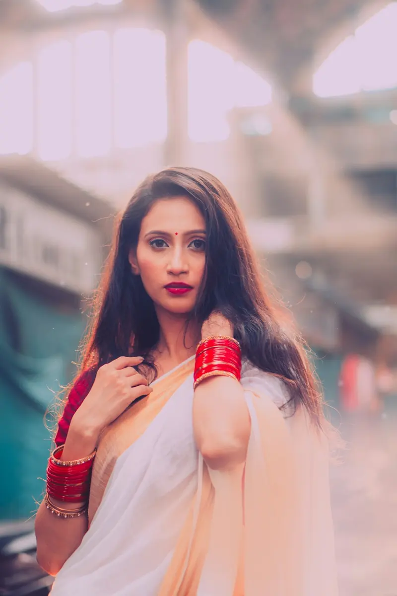 Woman in a white saree holding the pallu at her shoulder with bangles on her wrist