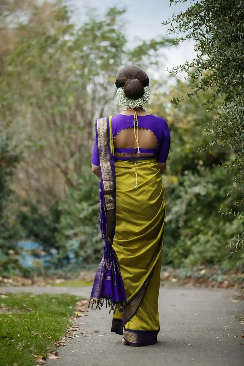 Woman in a green saree with a purple blouse walking away on a path, seen from behind