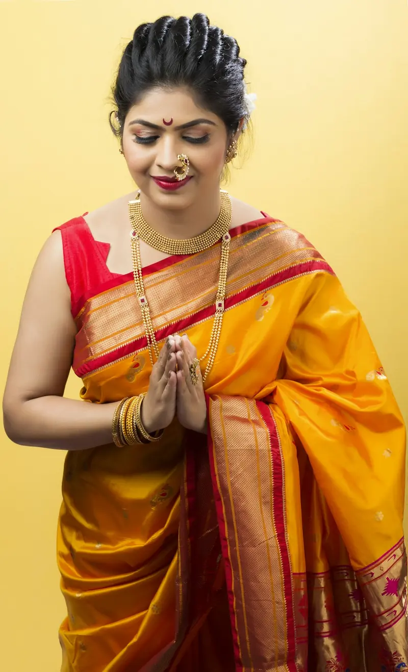 Woman in a yellow and red Paithani saree with folded hands in a namaste, smiling